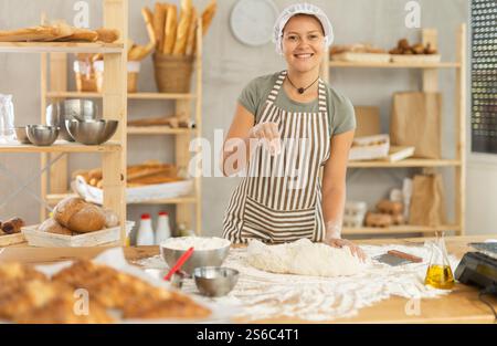 Frau arbeitet in der Bäckerei als Bäckerin, knetet Teig, arbeitet mit Mehl. Stockfoto