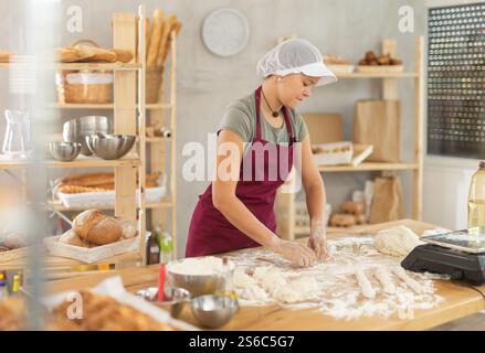 Mädchen arbeitet als Bäckerin in Bäckerei, formt Würstchen aus Teig, rollt lange runde Streifen aus Teig Stockfoto