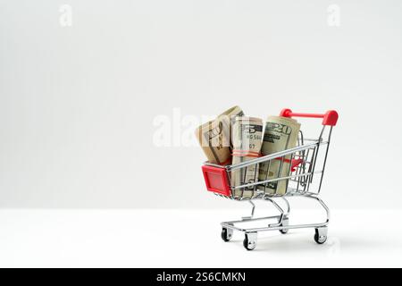 Roter Miniatur-Einkaufswagen gefüllt mit US-Dollar-Banknoten isoliert auf weißem Hintergrund, Konzept der Inflation oder Budgetierung Stockfoto