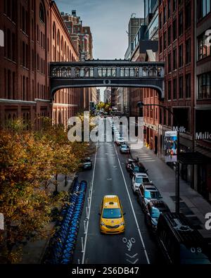 Mit dem gelben Taxi fahren Sie die West 15th Street entlang, eingerahmt von roten Backsteingebäuden und der Brücke am Chelsea Market. Vom Highline Park aus aufgenommen, ein wahrer New Yorker Moment. Stockfoto
