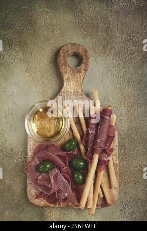 Eine Vorspeise aus Schinken, grissini und Oliven, serviert auf einem Holzbrett mit Olivenöl Stockfoto