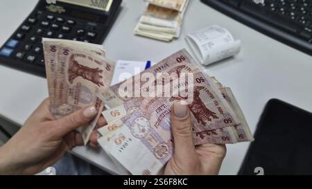 UNGHENI, MOLDAWIEN - 18. DEZEMBER 2024 Buchhalterin aus der Nähe, die mit einem Taschenrechner Geld über dem Schreibtisch zählen. Stapel der Moldawien-50-Lei-Banknote Stockfoto