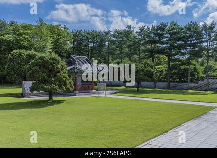 Kleiner Pavillon inmitten grüner, gepflegter Rasenflächen und Bäume unter klarem Himmel am 700 Patriots Memorial in Geumsan, Südkorea, Asien Stockfoto