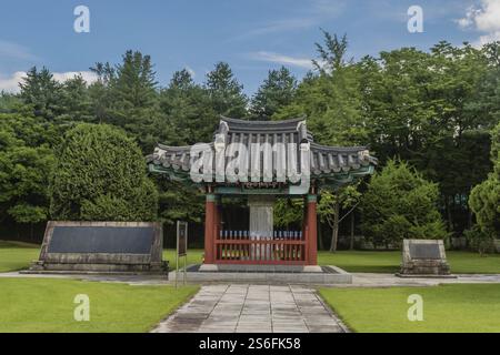 Ein Pavillon mit Steintafeln steht auf einem Rasen, umgeben von Bäumen unter blauem Himmel, am 700 Patriots Memorial in Geumsan, Südkorea, Asien Stockfoto