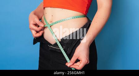 Eine glückliche schlanke Frau in Kleidung mit Maßband auf farbigem Hintergrund. Das Konzept eines gesunden Körpers, Körperpositivität. Panorama-Banner. Stockfoto