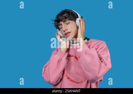 Junger Mann mit rosafarbenem Sweatshirt, der Musik mit kabellosen Kopfhörern hört, die Augen geschlossen, den Klang genießt Stockfoto