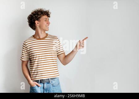 Junger Mann in einem gestreiften Hemd, der seitlich gegen eine einfarbige Wand zeigt, in einer hellen und lässigen Inneneinrichtung Stockfoto