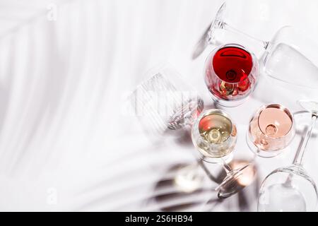 Drei Weingläser gefüllt mit Rot-, weiß- und Rosenwein, anmutig auf einem hellen, minimalistischen Hintergrund. Eine lebendige Darstellung der Vielfalt der Weine Stockfoto