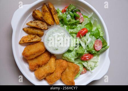 Nuggets, gebackene Kartoffelscheiben und Salat auf einem weißen Teller. Stockfoto