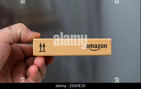 Paris, Frankreich - 22. November 2021: Ein kompaktes Kartonpaket mit Amazon-Markenzeichen, das in der Hand gehalten wird und die Pfeilsymbole nach oben zeigt, um die Orientierung zu erleichtern, mit einem neutralen Element Stockfoto