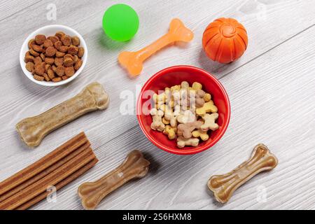 Trockenfutter und spielerisches Spielzeug für Hunde. Granuliertes Tierfutter in Schüsseln und künstliches Hundekauen mit Vitaminen. Bälle, ein Kauknochen auf dem Kaugummi Stockfoto