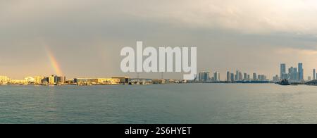 Abu Dhabi, VAE - 3. Januar 2025: Panoramablick auf die Skyline von Abu Dhabi mit einem doppelten Regenbogen, der über der Stadtlandschaft erscheint und die Mischung widerspiegelt Stockfoto