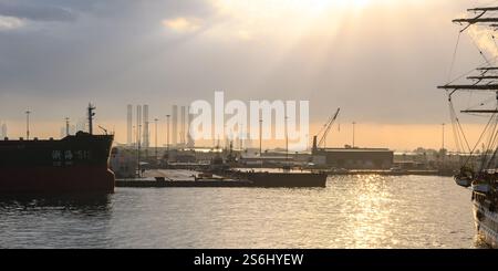 Abu Dhabi, VAE - 3. Januar 2025: Ein ruhiger Blick auf den Hafen bei Sonnenuntergang, mit Industriebauten und Schiffen, die vor dem goldenen Himmel stehen. Stockfoto