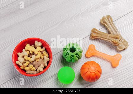 Trockenfutter und spielerisches Spielzeug für Hunde. Tierfutter in einer Schüssel und künstlicher Hund kauen Knochenfutter mit Vitaminen. Bälle und ein Kauknochen auf dem Boden. Oben Stockfoto