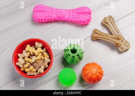 Trockenfutter und spielerisches Spielzeug für Hunde. Tierfutter in einer Schüssel und künstlicher Hund kauen Knochenfutter mit Vitaminen. Bälle und ein Kauknochen auf dem Boden. Oben Stockfoto