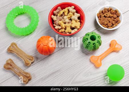 Trockenfutter und spielerisches Spielzeug für Hunde. Granuliertes Tierfutter in Schüsseln und künstliches Hundekauen mit Vitaminen. Bälle, ein Gummiring und ein Kaugummi Stockfoto