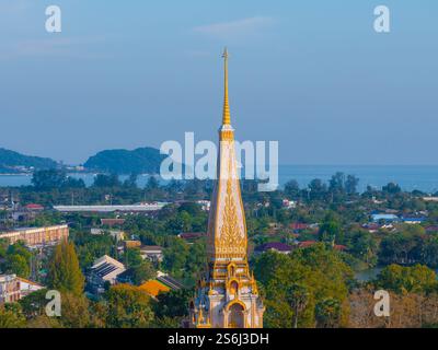 Der Tempel Wat Chalong in Phuket, Thailand, verfügt über einen goldenen Turm, komplizierte Details, üppiges Grün, ferne Hügel und eine ruhige Küste im Backgr Stockfoto