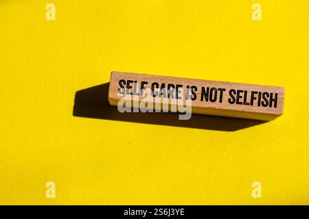 Selbstfürsorge ist keine egoistische Botschaft auf Holzblock auf gelbem Hintergrund. Konzeptionelle Selbstfürsorge ist kein egoistisches Symbol. Kopierbereich. Stockfoto