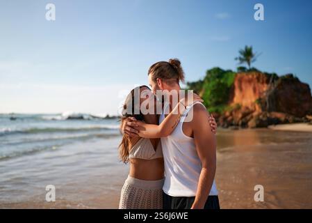 Liebevolles Paar umarmt sich am Sandstrand, ruhiges Meer. Mann, Frau teilen Kuss, friedliche Küstenszene. Intime Momente, Paare genießen romantischen Urlaub Stockfoto