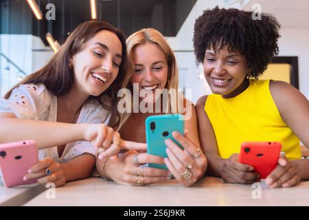 Drei Frauen, die sich mit Smartphones in einem modernen Café unterhalten Stockfoto