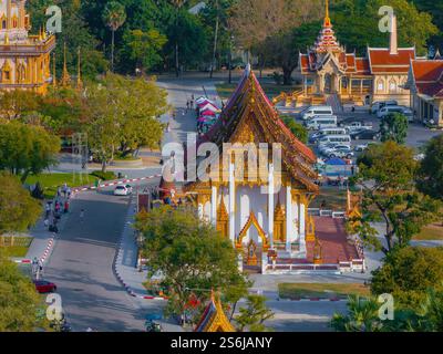 Der Tempel Wat Chalong in Phuket, Thailand, besticht durch traditionelle thailändische Architektur, üppige grüne Umgebung und einen Parkplatz mit sichtbaren Fahrzeugen. Stockfoto