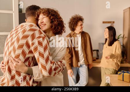 Mittlere Nahaufnahme einer jungen Erwachsenen, kaukasischen, die weit lächelt, während sie ihren nicht erkennbaren männlichen Freund umarmt Stockfoto