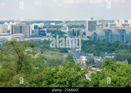 Panoramablick auf Kiew Stadt mit modernen Gebäuden, städtischem Grün und belebter Hauptstraße. Luftaufnahmen des Stadtbildes. Stadtentwicklung und Transp Stockfoto