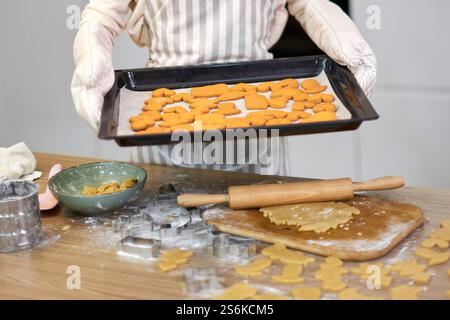 Hausfrau in Schürze hält Kekse auf Backblech in der Küche Stockfoto