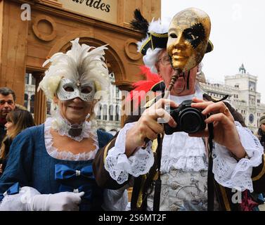 VENEDIG, ITALIEN - 14. FEBRUAR 2015: Zwei Senioren in Masken machen Fotos am Markusplatz während des traditionellen Karnevals. Stockfoto