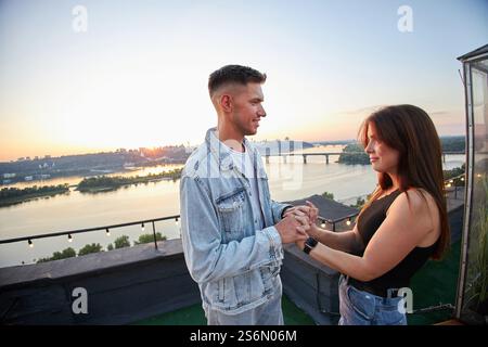 Ein junges Paar genießt einen ruhigen Abend auf einem Dach, umgeben von den warmen Farbtönen der untergehenden Sonne. Ihre Umarmung spricht von gemeinsamen Momenten und Ruhe Stockfoto