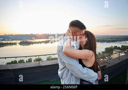 Ein junges Paar genießt einen ruhigen Abend auf einem Dach, umgeben von den warmen Farbtönen der untergehenden Sonne. Ihre Umarmung spricht von gemeinsamen Momenten und Ruhe Stockfoto