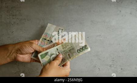 Person, die tschechische Kronen-Banknoten vor einem Betonhintergrund zählt, mit sichtbaren Händen und Fingern. Stockfoto