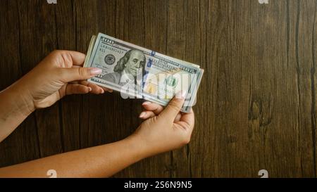 Eine Frau, die einen Stapel amerikanischer 100-Dollar-Scheine vor hölzernem Hintergrund hält und Währungsumschlag und Finanzkonzepte zeigt. Stockfoto