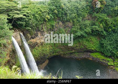 Wailua Falls auf Kauai, Hawaii, mit zwei Wasserfällen, die sich in einen ruhigen Pool stürzen, umgeben von üppigem Grün und dramatischen Klippen. Stockfoto