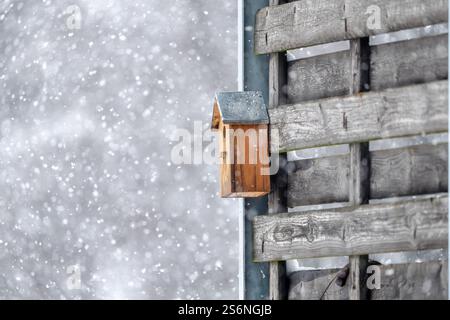 Ein Vogelhaus sitzt auf einem Holzzaun im Schnee. Das Vogelhaus ist klein und braun, und es ist von viel Schnee umgeben. Das Bild hat ein Friedensfu Stockfoto