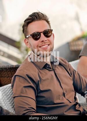 Portrait Bild der junge Mann im blauen Hemd in die Kamera schaut. Gut aussehender Geschäftsmann Sonnenbrille tragen. Gut aussehenden Mann lächelnd. Stockfoto