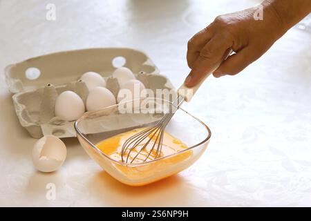Frau, die rohe Eier mit einem Schneebesen in Rührei schlägt Stockfoto