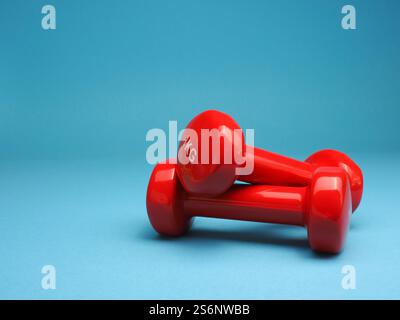 Rote Kurzhanteln auf blauem Hintergrund, Platz für Text, Fitness- oder Diätkonzept Stockfoto