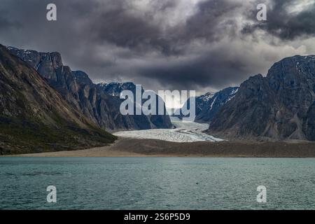 Dramatische Wolken schweben über dem Kangerlussuaq-Fjord, mit Bergen, die einen weitläufigen Gletscher umrahmen und ruhigen Gewässern, die die Landschaft widerspiegeln. Stockfoto