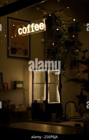 Von außen betrachtet, begrüßt das leuchtend weiße Neonschild des Coffee Shops die Besucher mit seiner Wärme. Hinter dem Glas, der beleuchtete Dessertkühlschrank hin Stockfoto