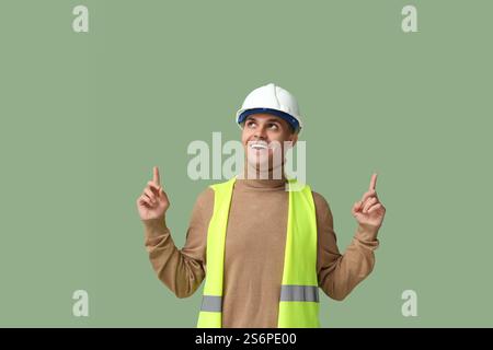 Junger männlicher Ingenieur, der auf etwas auf grünem Hintergrund zeigt Stockfoto