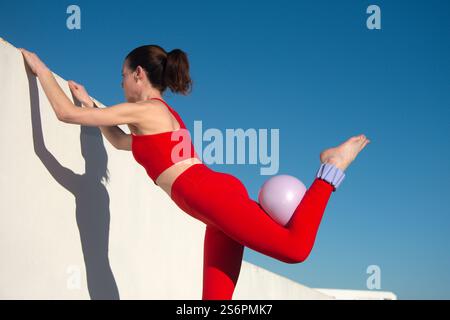 Frau, die Beinübungen macht, mit verstellbaren Knöchelgewichten und einem Pilatesball, Stockfoto