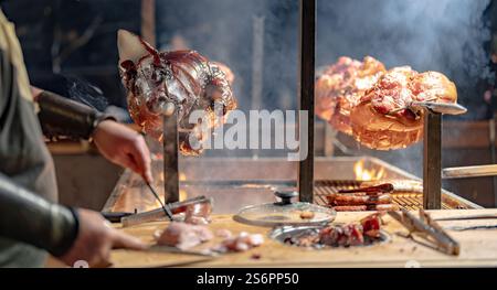 Ein Mann kocht Fleisch auf einem Grill. Das Fleisch wird am Spieß gekocht. Der Mann schneidet das Fleisch mit einem Messer ab Stockfoto