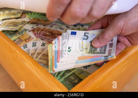 Die Hand des Mannes legt Euro-Scheine unter die Matratze, symbolisches Image, Geldversteck, Sparen, Altersvorsorge, Stockfoto