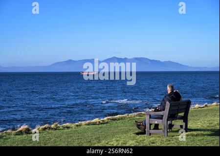 2 Personen sitzen auf einer Bank und blicken von Troon, South Ayrshire, Schottland, Großbritannien, Europa auf den Firth of Clyde zur Insel Arran Stockfoto