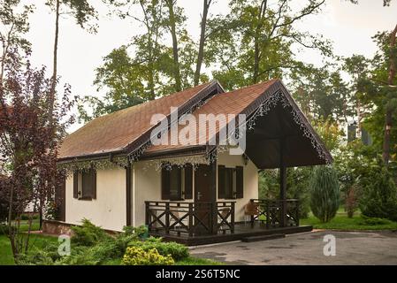 Gemütliches Haus mit einer charmanten Veranda, eingebettet zwischen ruhigem Grün und Bäumen, Hervorhebung der malerischen Architektur, Entspannungskonzept Stockfoto