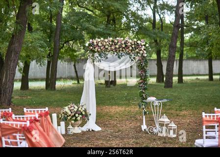 Hochzeitsbogen mit Blumen und weißen Vorhängen, Stühle im natürlichen Garten, zauberhafte Atmosphäre, festliches Szenenkonzept Stockfoto
