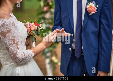 Bei einer Zeremonie im Freien tauscht die Braut Eheringe aus und hält gleichzeitig den Blumenstrauß elegant und feiert das Konzept der Liebe und des Engagements Stockfoto