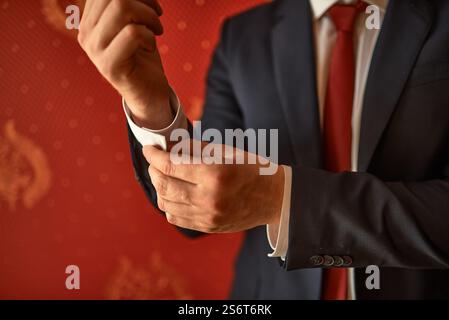 Geschäftsmann passt Manschettenknöpfe an einem strahlend weißen Hemd an und trägt dabei ein elegantes Anzug-Ensemble in einer eleganten Umgebung, professionelles Bekleidungskonzept Stockfoto