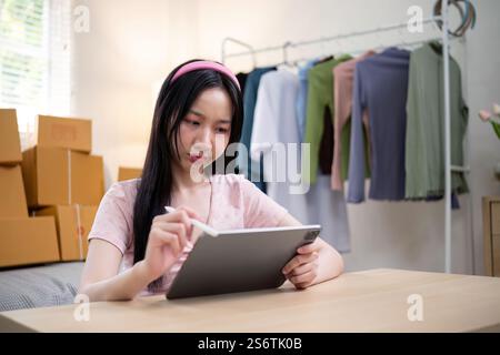 Junge Unternehmerin, die ihr E-Commerce-Bekleidungsgeschäft mit einem Tablet zu Hause verwaltet Stockfoto